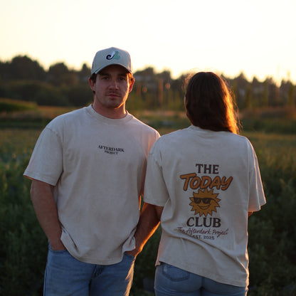 Man and woman wearing AfterDark Project “The Today Club” graphic t-shirts standing in a scenic outdoor field during golden hour — modern unisex Canadian streetwear for everyday wear.